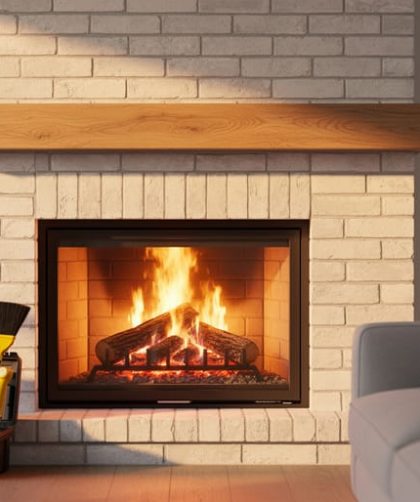 Renovated fireplace with whitewashed brick surround and natural wood mantel glowing with a fire, photographed straight-on at eye level; blurred background shows cozy seating and a neatly arranged chimney inspection toolkit with brush and flashlight near the hearth.